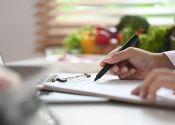 Professional nutritionist sitting at desk with fruit and vegetable working on diet plan.