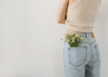 Young pretty woman with chamomile flowers bouquet in jeans pocket. Backside view